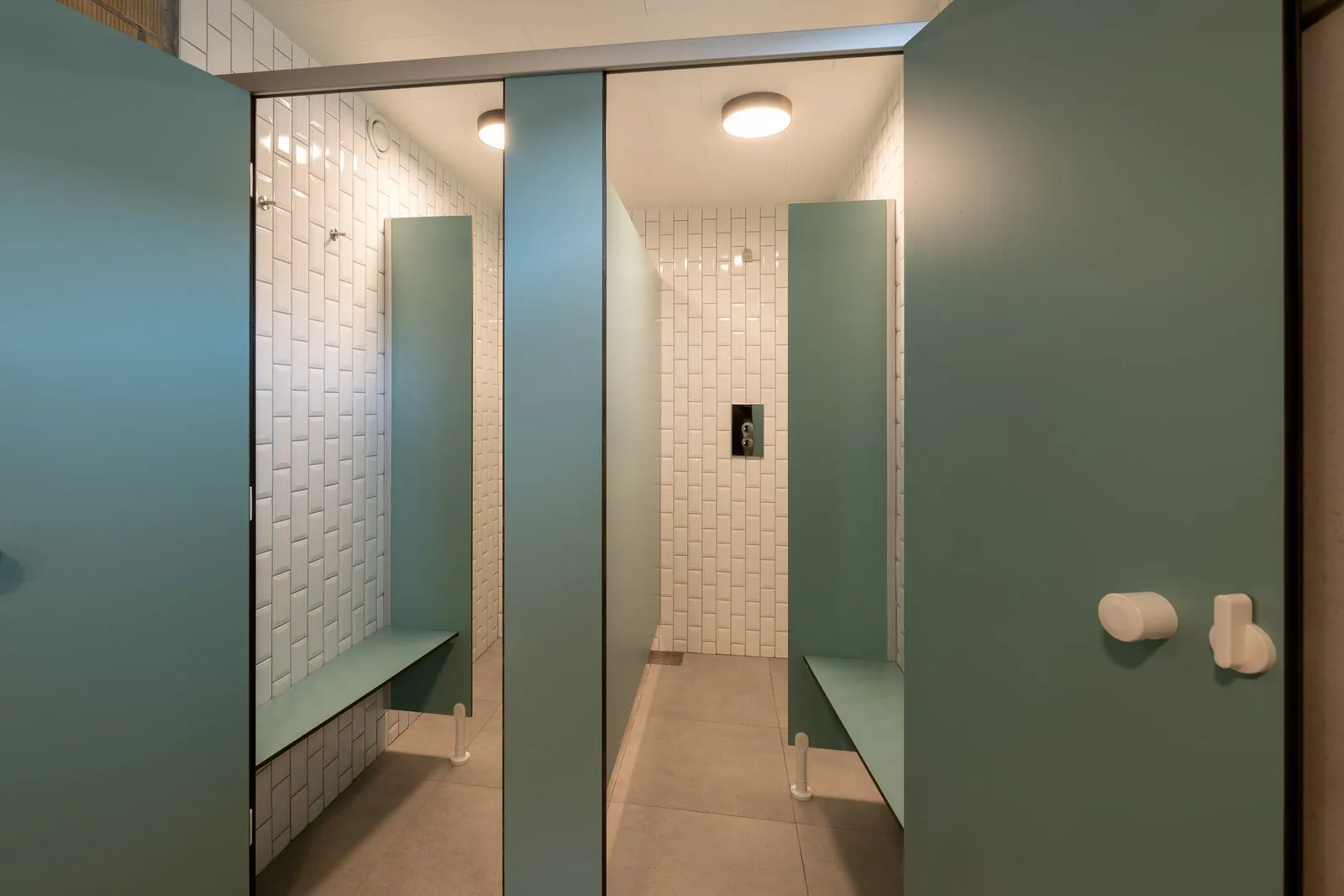 De doucheruimte met groene wanden, een tegelmuur en een bank om je spullen op te leggen