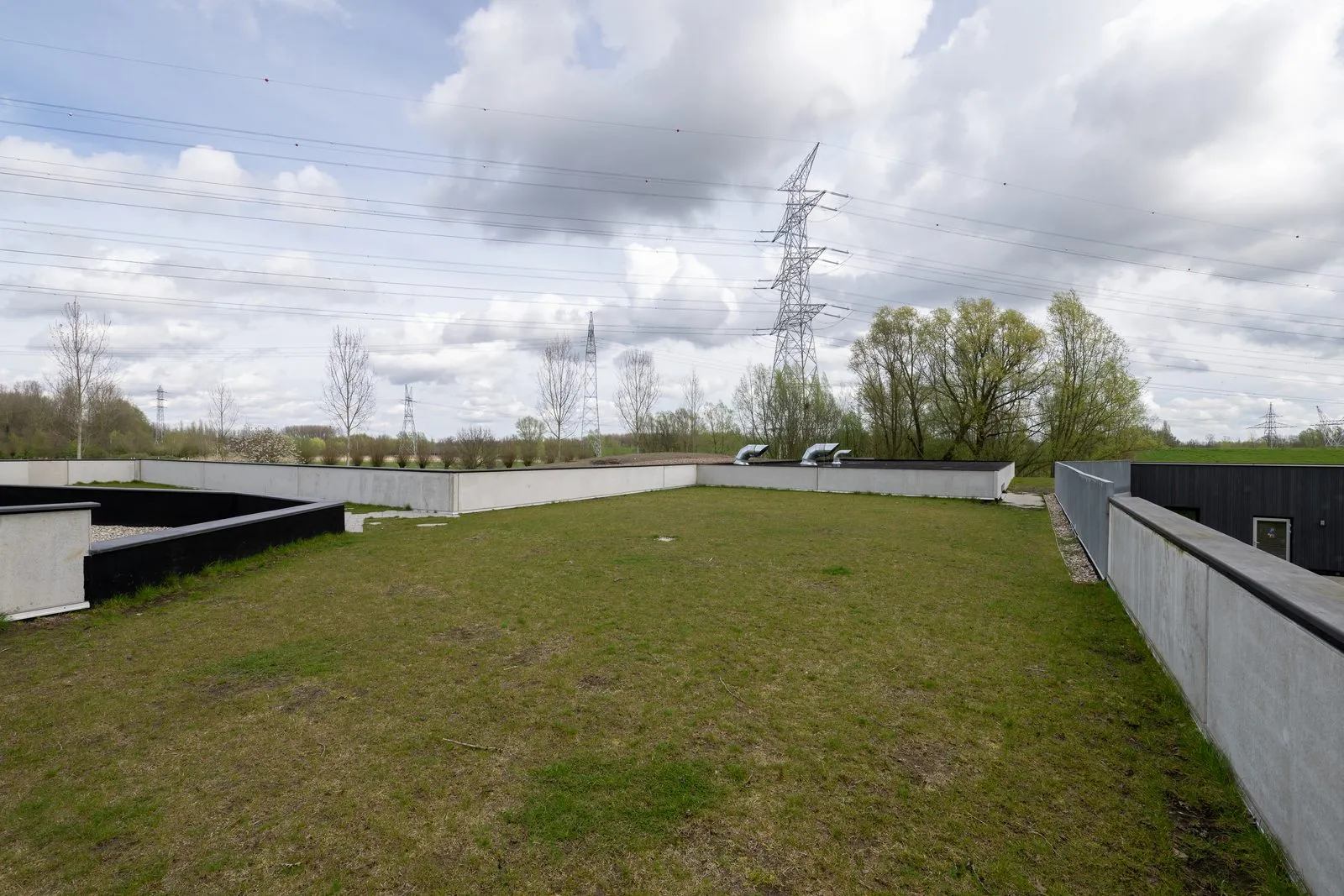 Het vlakke grasveld bovenop het gebouw, met zicht over de polder en een hoogspanningsmast in de verte