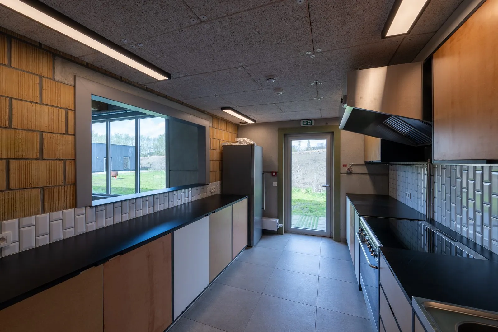 De keuken met zwarte werkbladen, een fornuis met dampkap en een grote opening in de muur die uitgeeft op de grote zaal