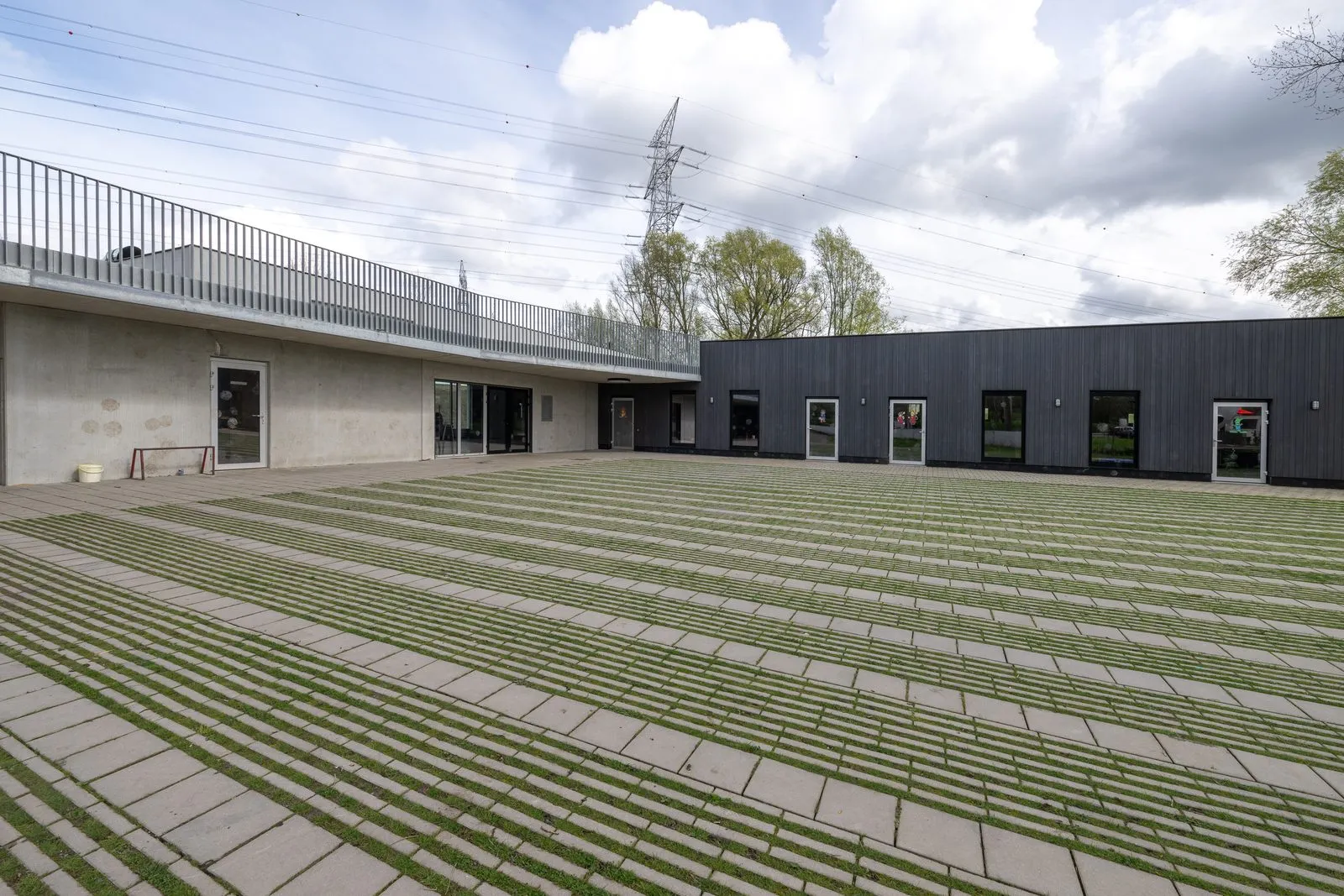 De binnenkoer van onze lokalen, met grasdoorgroeitegels en de zwarte houten gevel van de nieuwe vleugel