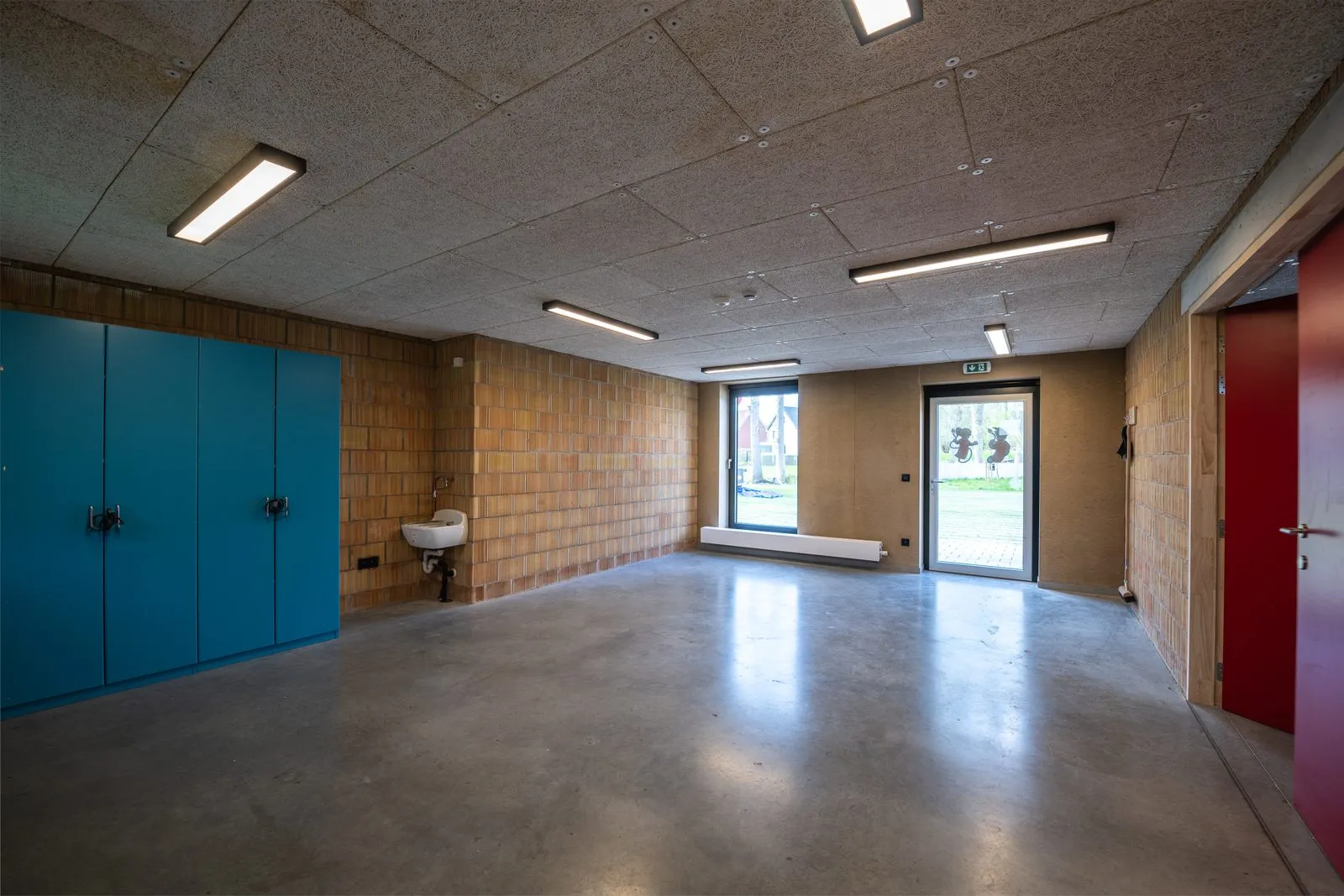 Een lokaal met een wasbak, een glazen deur naar buiten en blauwe kasten tegen de muur