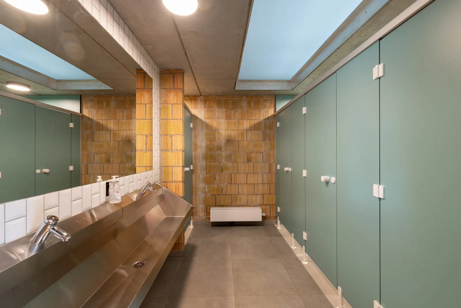 Het toiletblok, met een rij inox wastafels langs de tegelmuur en de cabines ernaast